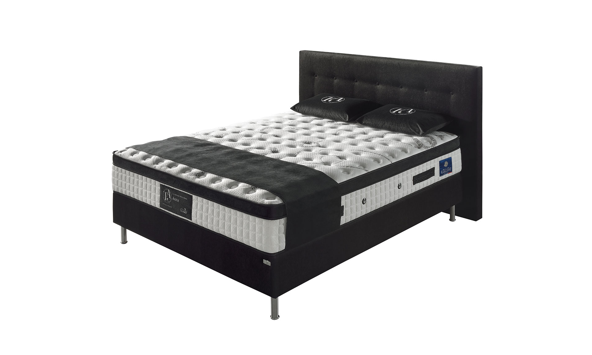 Photo présentant un lit composé d'un matelas à ressort de haute qualité blanc et noir de hauteur : 32, ainsi qu'une tête de lit en tissu noir et capitonné.