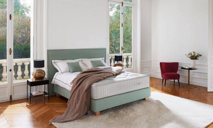 Photo présentant un lit composé d'un matelas ressort en saches blanc de hauteur : 30, ainsi qu'une tête de lit en tissu vert sauge avec capitonnage.