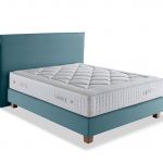 Photo présentant un lit composé d'un matelas ressort en saches blanc de hauteur : 30, ainsi qu'une tête de lit en tissu bleu argile avec capitonnage.