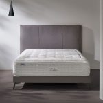 Photo présentant une chambre avec un lit composé d'un matelas de haute qualité blanc, ainsi qu'une tête de lit en tissu gris.