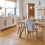 Photo présentant une salle à manger avec une table carré, chaise tissu, un buffet haut et un bahut. Chaque meuble à une finition en chêne massif blond et une peinture couleur argile.