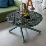 Photo d'une table ronde fermée en céramique verre brillant effet marbre noir avec des veines vertes. Elle est en table basse modifiable en table à manger.